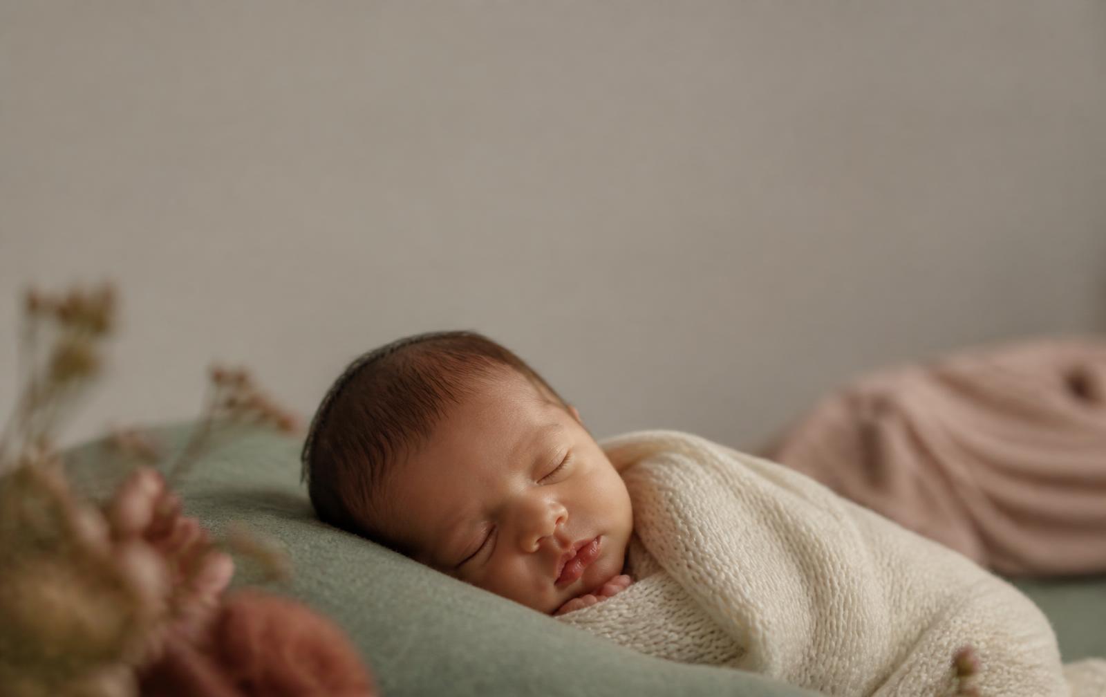 A newborn sleeping peacefully wrapped in a cream blanket